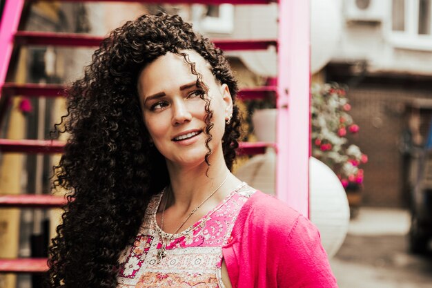 Beau modèle souriant avec une coiffure afro curls vêtue de vêtements hipster roses