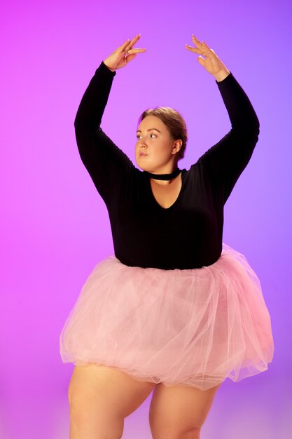 Beau modèle de taille plus caucasien pratiquant la danse de ballet sur un studio violet rose dégradé