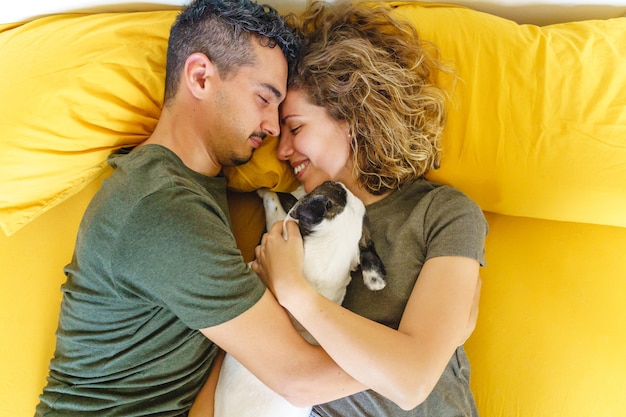 Beau moment intime de couple avec animal de compagnie sur le lit. Vue de dessus horizontale serrant le chien à l'intérieur.