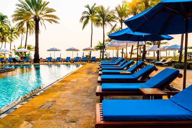 beau palmier avec chaise parapluie piscine dans un hôtel de luxe au lever du soleil - concept de vacances et de vacances