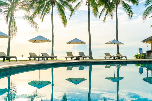 Beau parasol de luxe et chaise autour de la piscine extérieure dans l'hôtel et la station balnéaire avec cocotier sur ciel coucher de soleil ou lever de soleil - vacances et concept de vacances