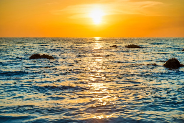 Beau paysage de coucher de soleil coloré avec plage de sable, soleil doré et pierres au bord de la mer