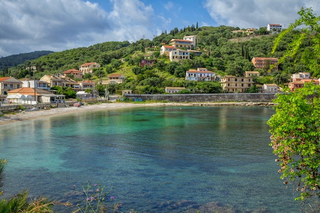 Beau paysage d'été de la station balnéaire aux eaux turquoises, village aux maisons colorées et montagnes à l'horizon et ciel bleu. Île de Corfou, Grèce.