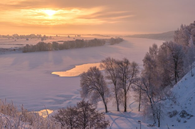 Beau paysage d'hiver. Lever du soleil sur la rivière. Arbres enneigés au bord de la rivière.