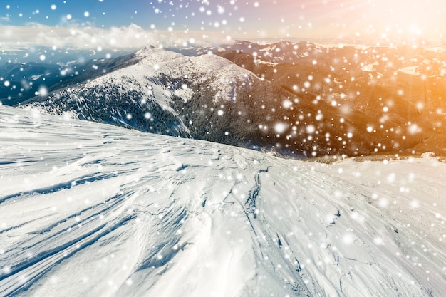 Beau paysage d'hiver. Pente raide de colline de montagne avec de la neige profonde blanche, panorama de la chaîne de montagnes lointaine, de grands flocons de neige et des rayons de soleil brillants brillants sur l'espace de copie coloré du ciel bleu