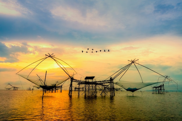 Beau paysage naturel lumière dorée du ciel du matin au lever du soleil avec une volée d'oiseaux survolant l'outil de pêche indigène, mode de vie rural au canal de Pakpra, Baan Pak Pra, Phatthalung, Thaïlande