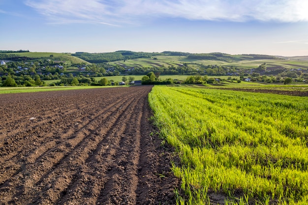 Beau paysage paisible au printemps large de champs labourés et verts éclairés par le soleil du matin qui s'étend à l'horizon sous un ciel clair sur les collines et le village lointains. Agriculture et concept agricole.