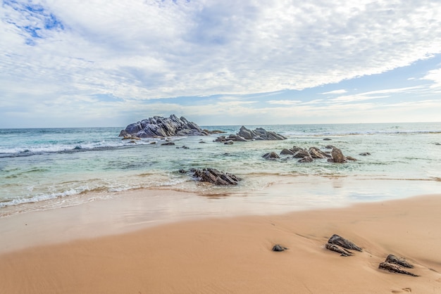Beau paysage d'une plage de sable avec des rochers dans l'océan sur un fond de ciel bleu.
