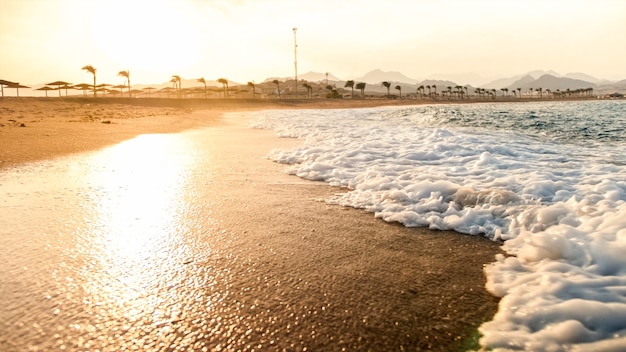 Beau paysage de vagues de l'océan se brisant sur le rivage contre le soleil couchant dans le ciel. Arrière-plan parfait pour votre voyage de vacances d'été