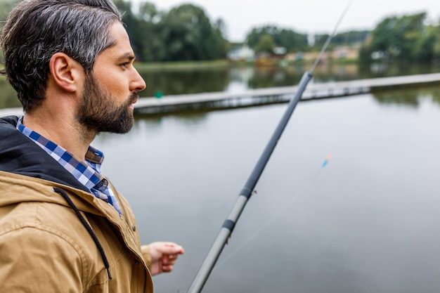 Beau pêcheur pêchant avec une canne sur le lac