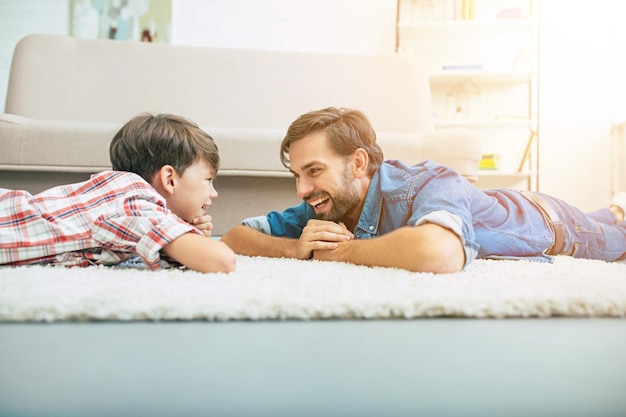 Beau père heureux et son fils souriant sont allongés sur le sol à la maison ensemble