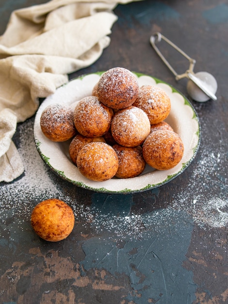 Photo beau petit déjeuner. boules de beignets au fromage cottage avec du sucre en poudre sur un fond sombre. fermer. copier l'espace,