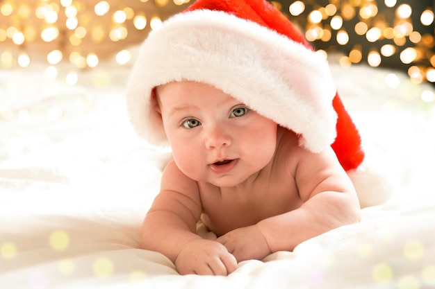 Beau petit enfant fête Noël. Les vacances du nouvel an. Un enfant en costume de Noël. Concept d'enfance et de personnes - heureux nouveau-né en bonnet de Noel sur fond de lumières de vacances.