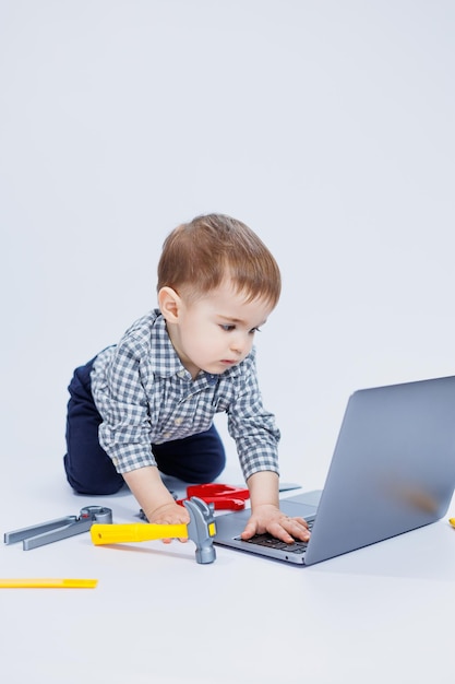 Un beau petit garçon de 23 ans en chemise sur fond blanc regarde un ordinateur portable Un enfant joue avec un ordinateur portable