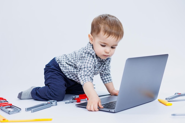 Un beau petit garçon de 23 ans en chemise sur fond blanc regarde un ordinateur portable Un enfant joue avec un ordinateur portable