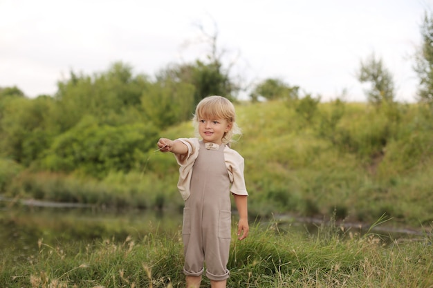 un beau petit garçon aux cheveux blonds et aux cheveux bouclés se repose dans la nature au bord de la rivière