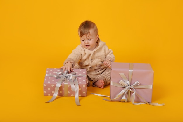 un beau petit garçon aux yeux bleus dans un costume chaud tricoté avec des coffrets cadeaux sur fond jaune