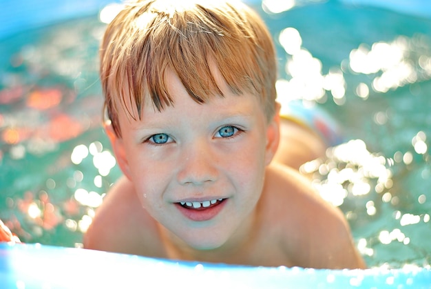 Beau petit garçon blond souriant aux yeux bleus dans la piscine