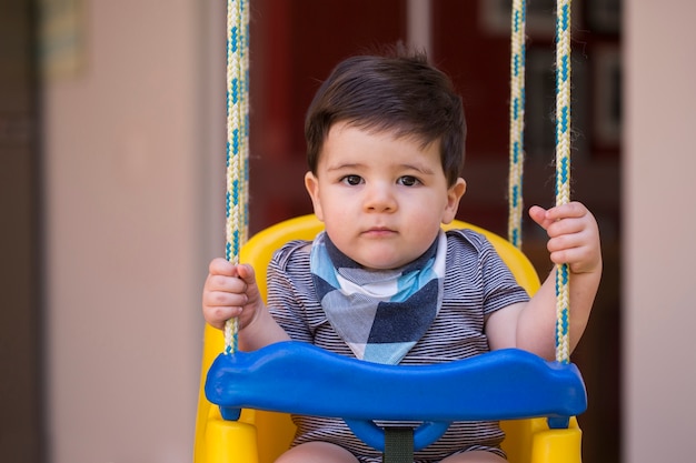 Beau petit garçon brésilien regardant la caméra. bébé sur la balançoire. Bébé heureux.