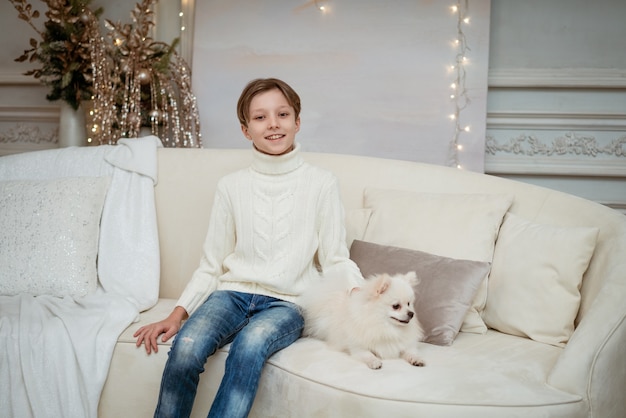 Beau petit garçon caucasien sur le canapé avec un chien blanc sur un fond de Noël clair joyeux chris...