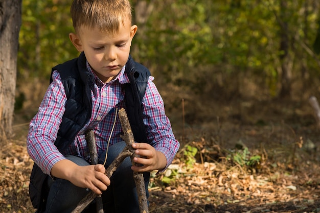 Beau petit garçon construisant un petit tipi à partir de brindilles et de branches en bois alors qu'il joue à l'extérieur dans les bois