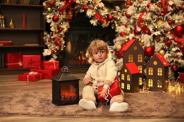 un beau petit garçon dans un costume d'hiver tricoté tient une boîte-cadeau de Noël et du nouvel an