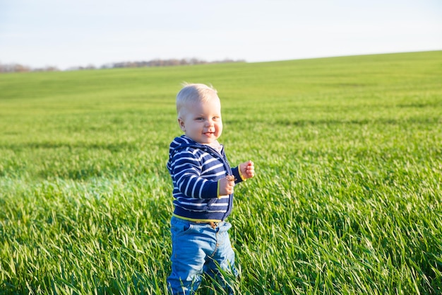 Beau petit garçon debout dans l'herbe verte sur le champ de printemps