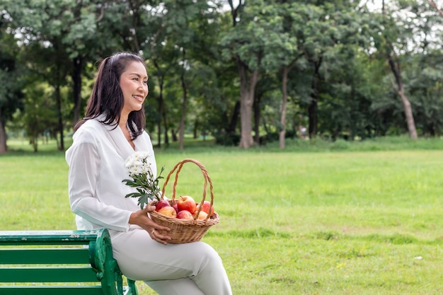 Beau portrait asiatique de femme senior avec corbeille de fruits et fleur dans le parc.