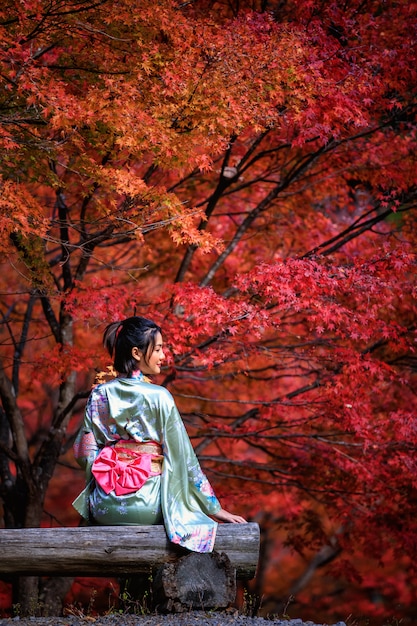 Beau portrait de femme asiatique portant un kimono d'or du Japon assis sur un banc en bois dans le parc