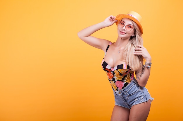 Beau portrait de femme blonde en maillot de bain avec des lunettes de soleil sur fond jaune