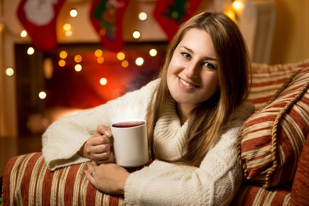 Beau Portrait De Femme Souriante Assise Avec Une Tasse De Thé Chaud à La Cheminée à La Veille De Noël