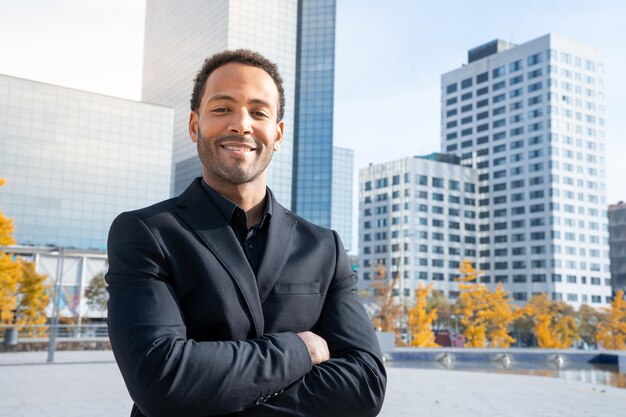 Beau portrait d'homme d'affaires souriant avec les bras croisés portant une suite avec la ville en arrière-plan