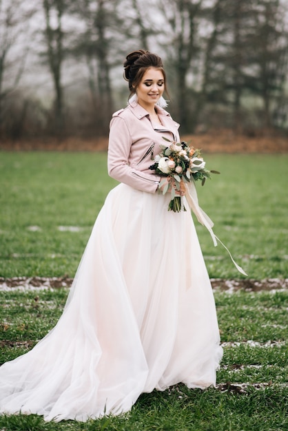 Un beau portrait de la mariée dans une robe élégante avec un bouquet d'hiver de roses, de coton et d'épinette contre un champ vert avec le premier. Photo de mariage