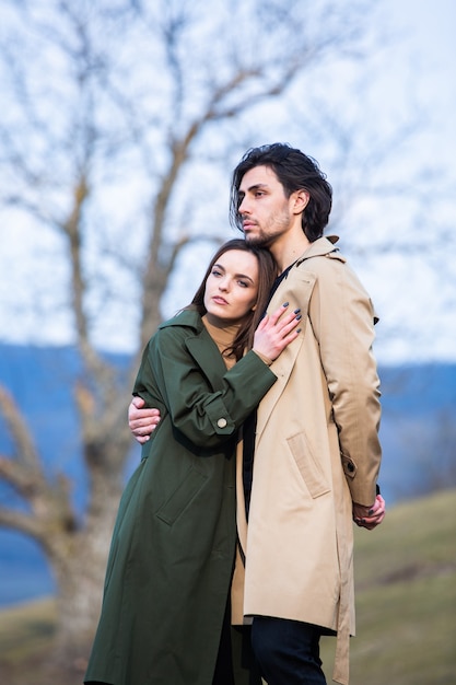 Beau portrait sensuel du jeune couple élégant amoureux Image de l'adorable couple brune en trench-coat de pluie dans le parc