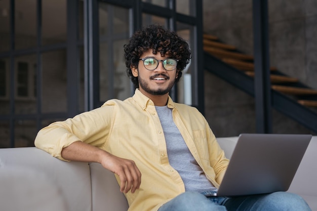 Beau programmeur indien confiant utilisant un ordinateur portable regardant la caméra travaillant à domicile