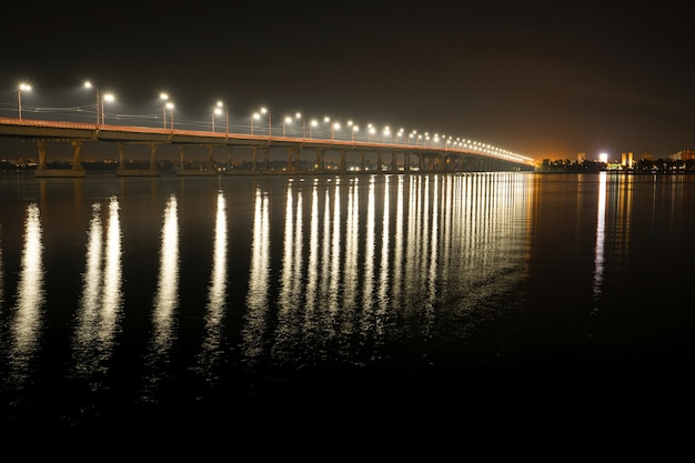 Beau reflet brillant de lanternes lumineuses avec une lumière froide dans le grand fleuve Dniepr sous un long pont qui le traverse