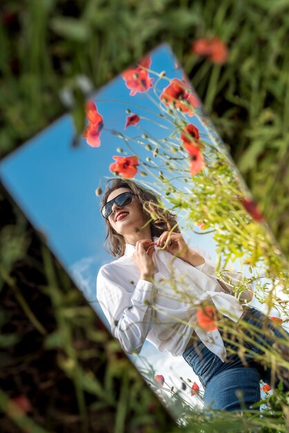 Beau reflet d'une fille dans le miroir sur un champ de coquelicots. heure d'été