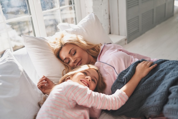 Beau rêveur. Mère et fille en vêtements de nuit souriant en position couchée sur le lit à la maison