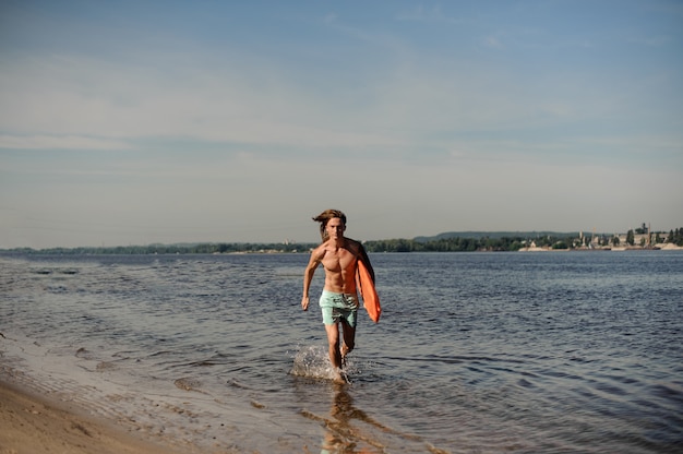 Beau sauveteur de plage sexy qui longe la rive du fleuve avec des équipements de sauvetage