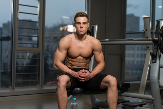 Beau et séduisant jeune homme avec un corps musclé relaxant dans la salle de sport