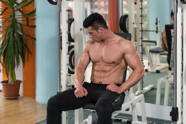 Beau et séduisant jeune homme avec un corps musclé relaxant dans la salle de sport