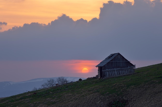 Beau soleil au coucher du soleil. Vieille maison en bois sur une colline de montagne. Bergers de résidence. Carpates, Ukraine, Europe