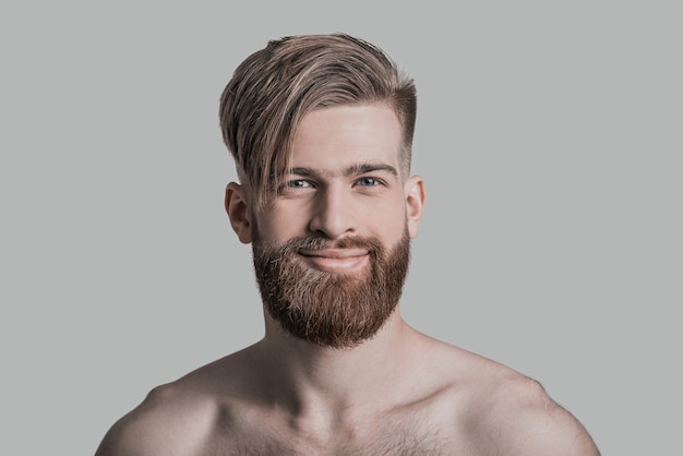 Beau sourire. Portrait d'un bel homme regardant la caméra et souriant en se tenant debout sur fond gris