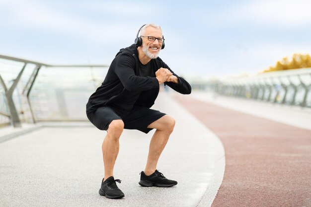 Beau sportif âgé motivé s'entraînant à l'extérieur en écoutant de la musique