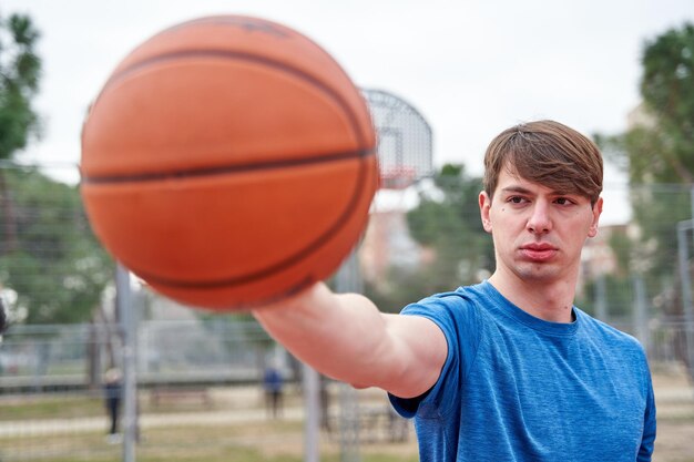 Beau sportif debout sur fond de terrain de basket avec basket à la main