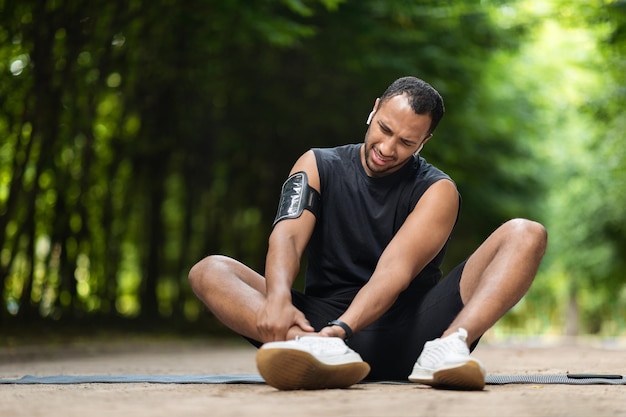 Beau sportif noir exerçant dans un parc public touchant la cheville