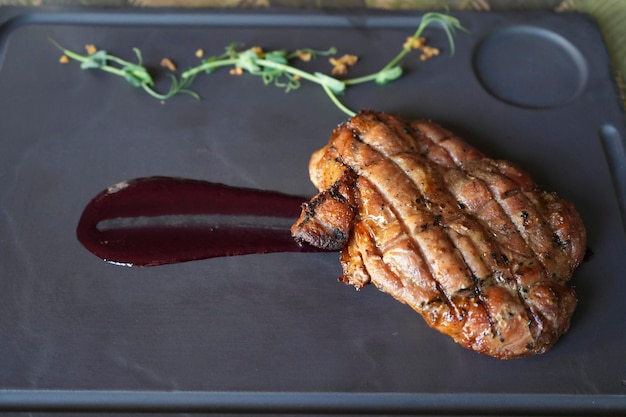 Beau steak de porc juteux avec de la sauce aux baies sur une assiette carrée en marbre Steak de viande fraîchement grillé