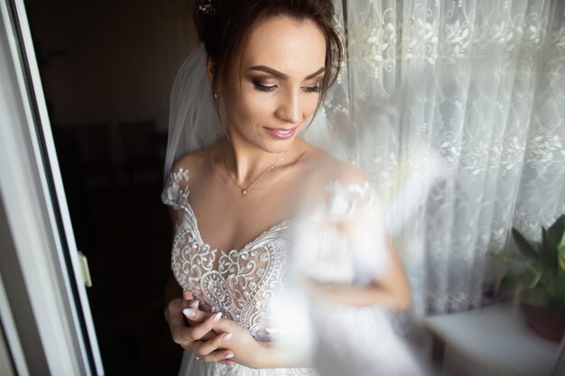 Beau style de mariée. Mariage fille debout dans la robe de mariée de luxe près de la fenêtre