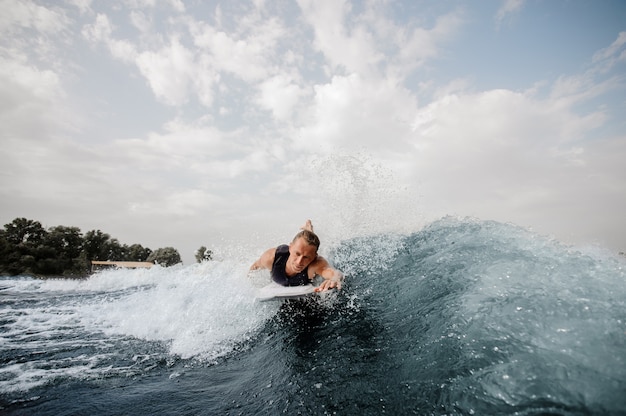 Beau surfeur allongé sur un tableau blanc et nageant sur la rivière