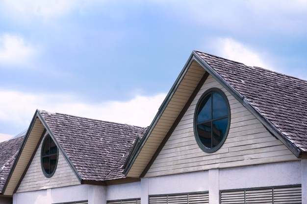 Beau toit de maison en bois avec une fenêtre ronde sur fond de ciel bleu